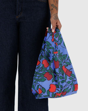 Person hält den Baby Baggu Einkaufsbeutel Apple Tree, klein und faltbar, mit fruchtigem Print, ideal für umweltbewusstes Einkaufen, passend zum vielseitigen Angebot von Human Empire Shop.