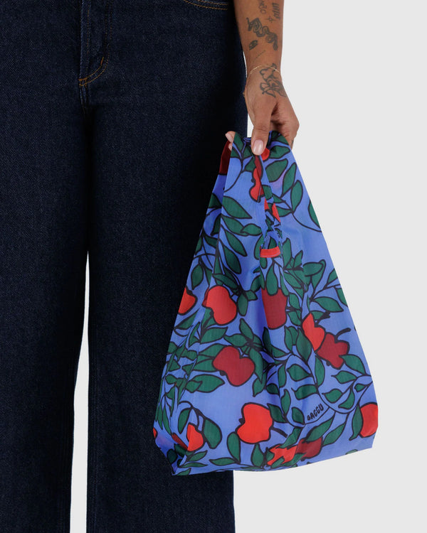 Person hält den Baby Baggu Einkaufsbeutel Apple Tree, klein und faltbar, mit fruchtigem Print, ideal für umweltbewusstes Einkaufen, passend zum vielseitigen Angebot von Human Empire Shop.