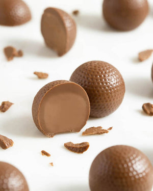 9 Milchschokoladekugeln mit Haselnusspralinenfüllung, präsentiert auf weißer Oberfläche, eine halbiert. Perfekte Geschenkidee aus traditioneller Handwerkskunst für Genießer.