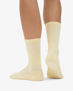 Ein Paar Füße trägt die Organic Active Socks Soft Yellow, gerippte Tennissocken mit nachhaltigem Design und extra Komfort, ideal für sportlichen Halt.