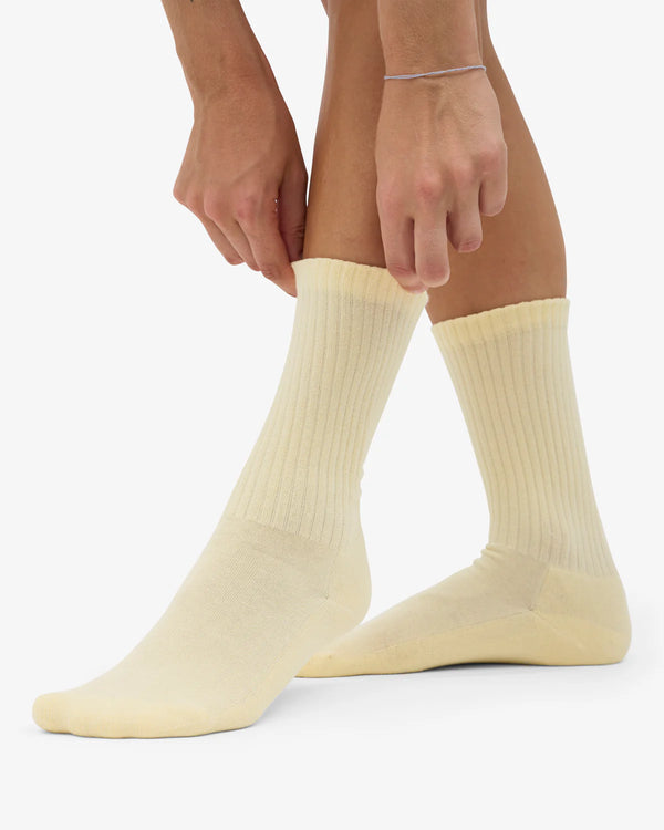 Nahaufnahme von Beinen in Organic Active Socks Soft Yellow, die jemand anpasst. Nachhaltige, gerippte Tennissocken mit extra Komfortsohle aus Bio-Baumwolle, hergestellt in Portugal.
