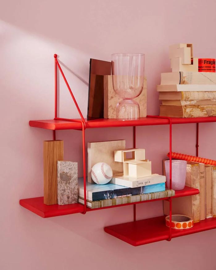 Shrink Regal Lobster: Wandregal aus rot lackiertem Buchenholz, stilvoll dekoriert mit Büchern, Vasen und Accessoires, bietet stilvolle Aufbewahrung in einem minimalistischen Design.