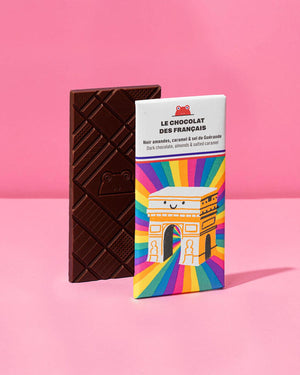 Triomphe Dunkle Schokolade mit Mandeln und gesalzenem Karamell 70g, zeigt geometrisches Froschmuster. Verpackung illustriert mit lachendem Arc de Triomphe von Carolina Buzio.