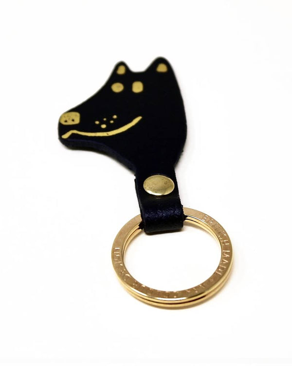 Schlüsselanhänger Dog Black aus schwarzem Leder, Hundekopf-Form mit goldenen Details, verbunden mit einem goldfarbenen Schlüsselring. Hergestellt in Schottland von Ark Colour Design.