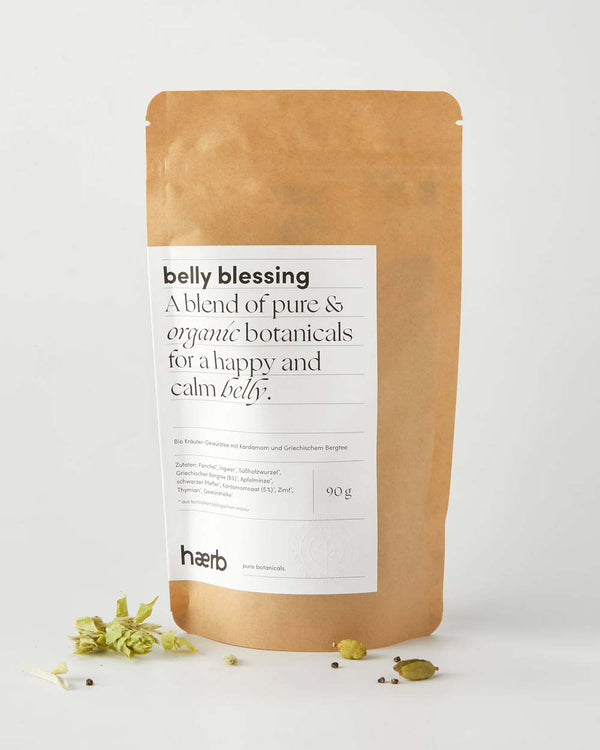 Haerb Bio Teemischung Belly Blessing - Kardamom und Griechischer Bergtee in kraftpapier Beutel, mit getrockneten Botanicals wie Kardamomkapseln und Pfefferkörnern im Vordergrund.