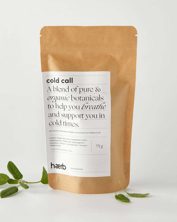 Kraftpapierbeutel mit Haerb Bio Teemischung Cold Call, einer Mischung aus biologischen Kräutern wie Salbei und Minzöl, dekoriert mit frischen Kräutern.