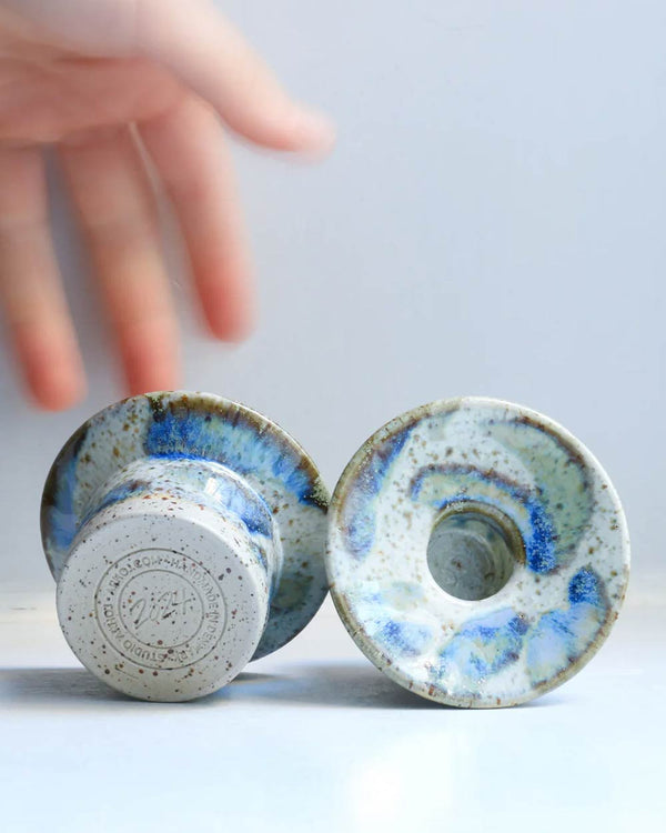 Zwei Hono Comet Rain Kerzenständer von Studio Arhoj, handgefertigt, einer zeigt den Stempel, der andere die Oberseite mit zentralem Loch, auf hellem Hintergrund.