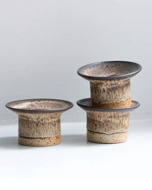 Drei handgefertigte Hono Pinyon Cone Kerzenständer aus Keramik von Studio Arhoj, mit erdigen Glasuren, zwei gestapelt, einer separat, vor grauem Hintergrund.