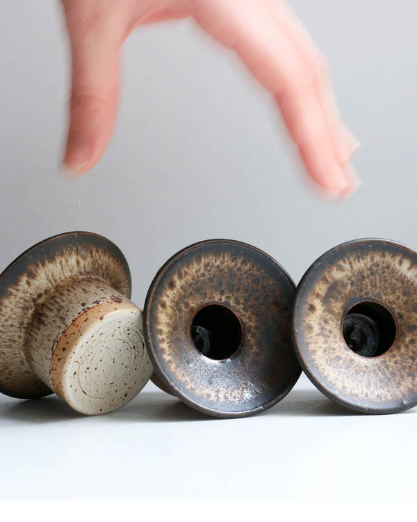 Drei handgefertigte Hono Pinyon Cone Kerzenständer von Studio Arhoj, mit flared Lippe und zentralem Loch, speckled Glasureffekt, auf einer flachen Oberfläche liegend.