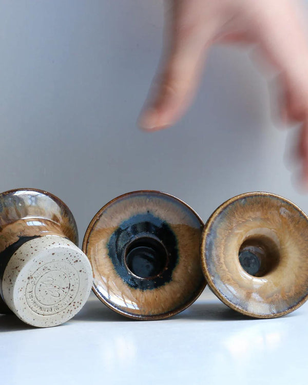 Drei Hono Root Beer Kerzenständer von Studio Arhoj; handgefertigte, glasierte Keramik mit unglasiertem Boden und Herstellermarke, ein Hand arrangiert einen Kerzenhalter.