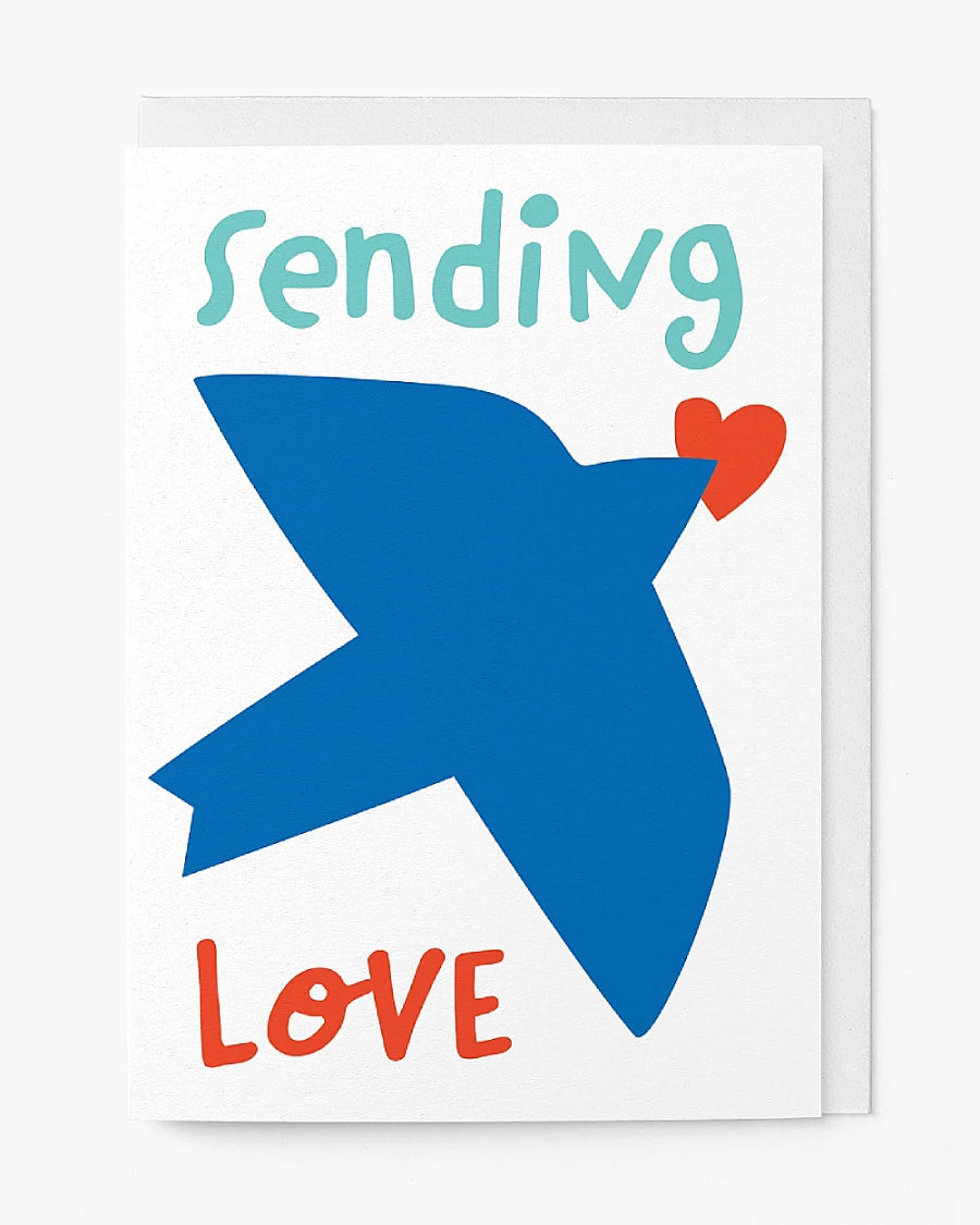 Sending Love Klappkarte zeigt einen blauen Vogel im Flug mit rotem Herz am Schnabel, handgeschriebenen Text in Teal und Rot; gefertigt aus nachhaltigem FSC-Papier.