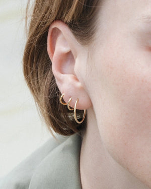 Nahaufnahme eines Ohrs mit drei goldenen Creolen. Produkt: Creolen Gold Gr. M, vergoldet und handgefertigt, von Jukserei, präsentiert im Human Empire Shop.