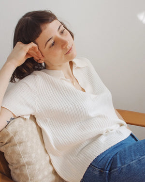 Person trägt Croissant Kette Gold von Jukserei, entspannend in einem Holzsessel sitzend, mit nachdenklichem Ausdruck. Kette aus 24 Karat vergoldetem Sterlingsilber sichtbar.