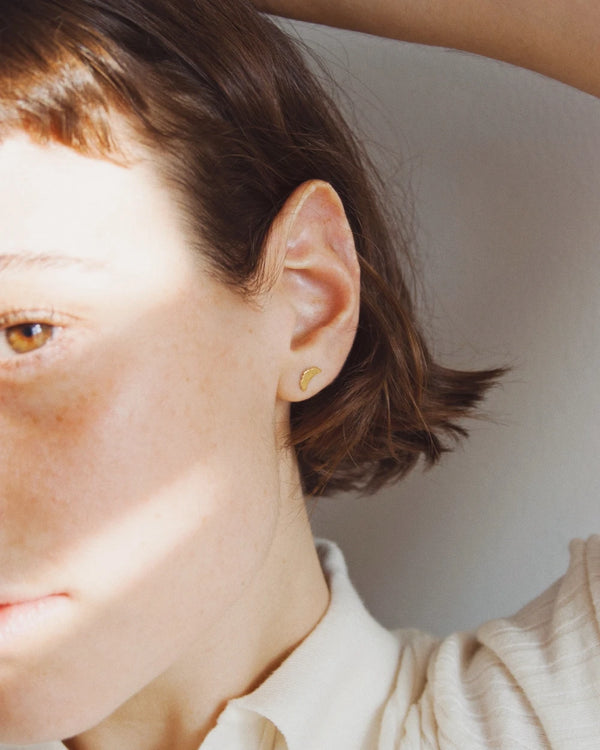 Nahaufnahme eines Croissant Ohrstecker Gold aus vergoldetem Sterlingsilber, getragen an einem Ohr. Schlichtes, elegantes Design, perfekt für einen stilvollen Akzent.