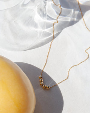 Picnic Kette Gold: Feine vergoldete Halskette mit fünf kleinen Goldperlen auf weißem Stoffhintergrund, von Jukserei, präsentiert im Human Empire Shop-Kontext.