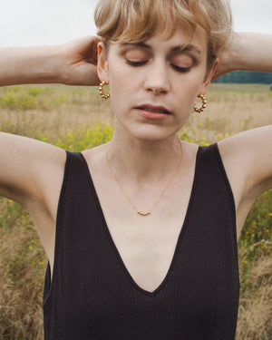 Frau trägt Picnic Kette Gold von Jukserei, zarte 24 Karat vergoldete Halskette mit Perlen, im Freien, umgeben von Natur, verkörpert eleganten, natürlichen Stil.