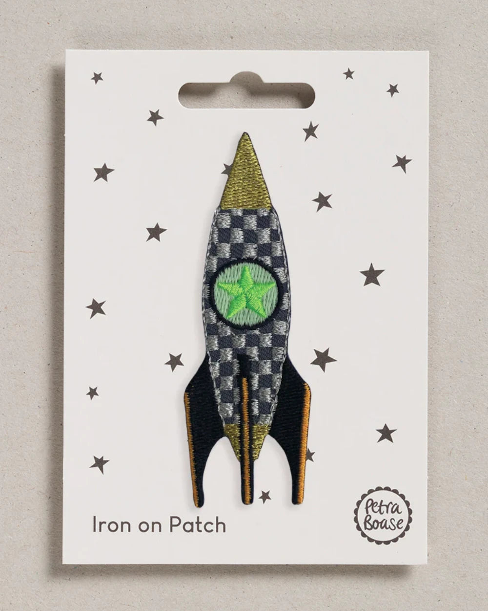 Rakete Aufnäher (zum Aufbügeln): Gestickter Patch in Raketenform mit grünem Fenster, schwarzem-goldenem Finnen, auf sternenbedrucktem Karton, Petra Boase Logo unten rechts.