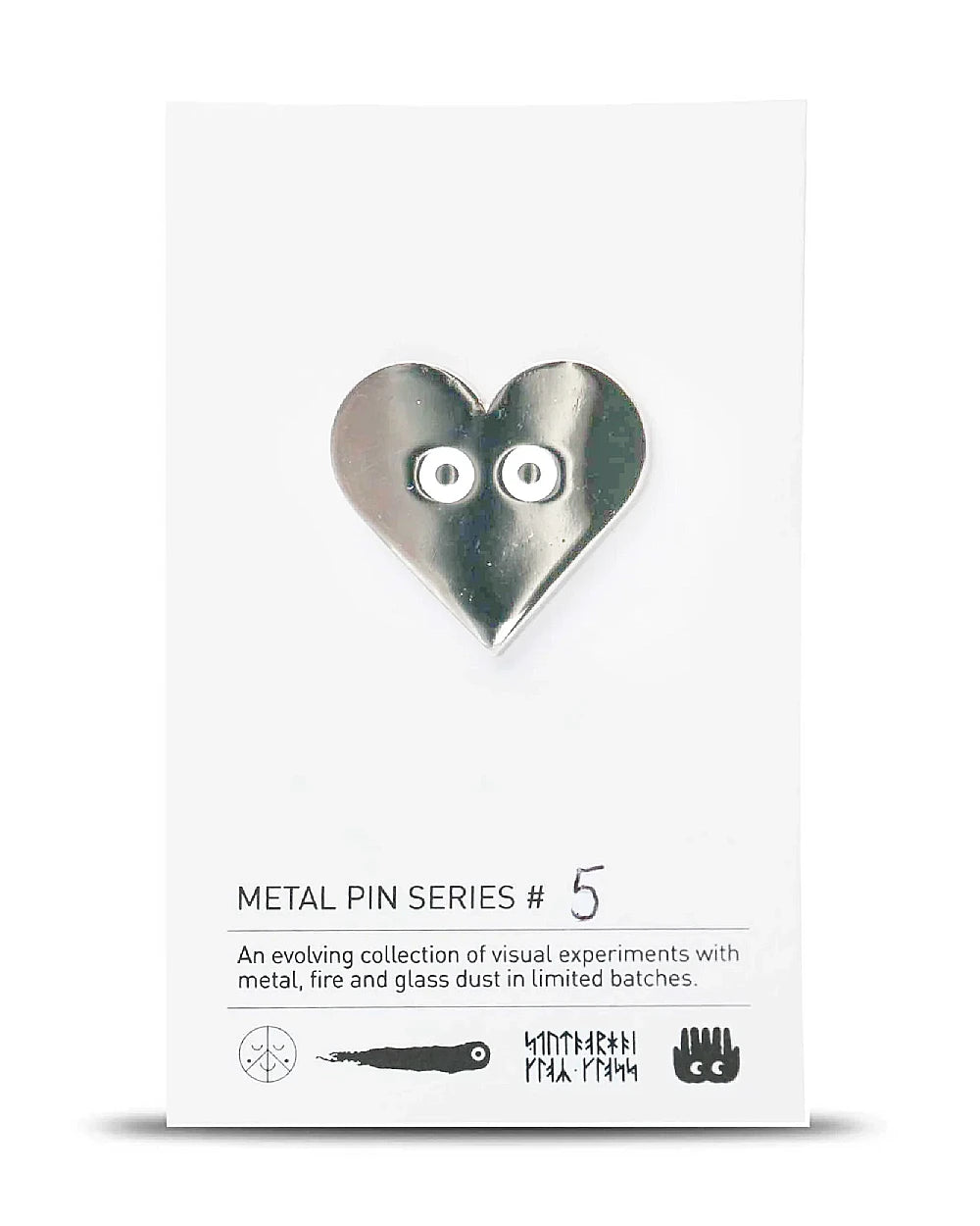 Metall-Pin Silver Heart (Serie #5) von Studio Arhoj: Herzform mit geprägten Augen, auf minimalistisch gestaltetem Trägerkarton, Teil einer limitierten Sammlungsreihe. Maße: 3 x 2,5 cm.