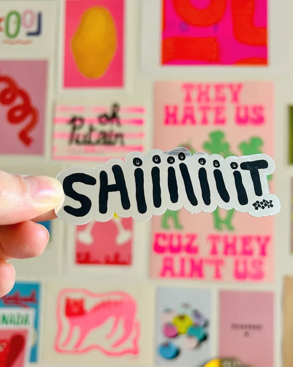Shiiiiiiiiiit Mirror Sticker mit cartoonhaften Buchstaben und lächelnden Gesichtern, entworfen von Marie Chanteur für Wobbly Studio, gehalten vor buntem Posterhintergrund.