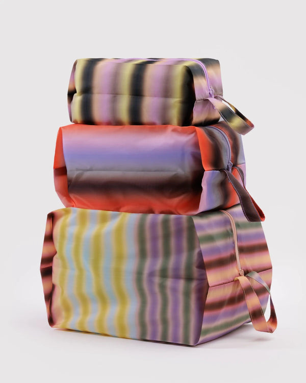 Baggu 3D Zip Set Gradient Stripes: Drei gestapelte, pastellfarbene Reißverschlusstaschen mit Trageschlaufen aus recyceltem Ripstop-Polyester, ideal zum Organisieren von Alltagsgegenständen.