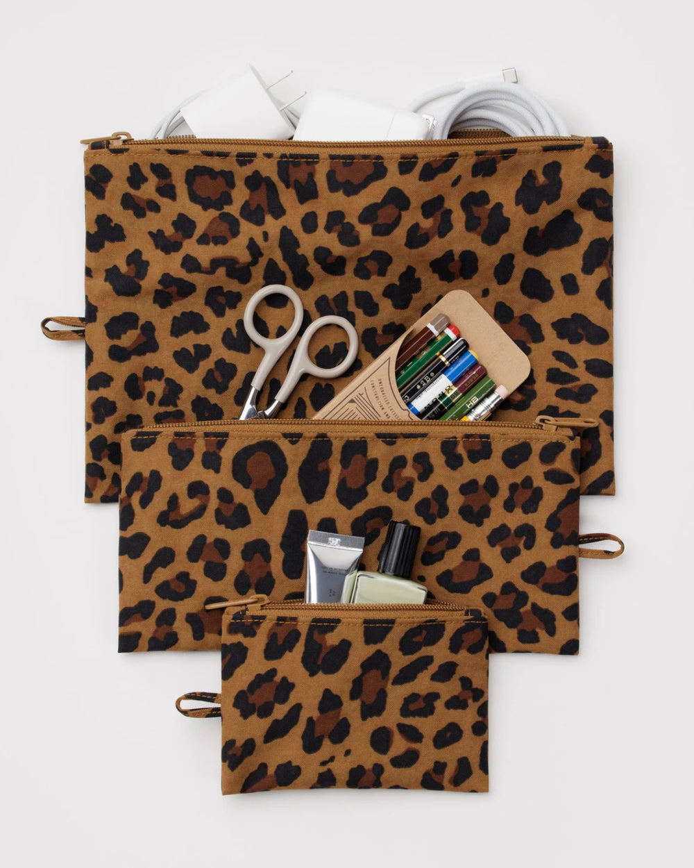 Baggu Flat Pouch Leopard (3teilig): Drei Reißverschlusstaschen mit Leopardendruck, ideal für Alltagsgegenstände. Gezeigt mit Elektronik, Schreibwaren und Kosmetik, aus robustem, recyceltem Nylon.