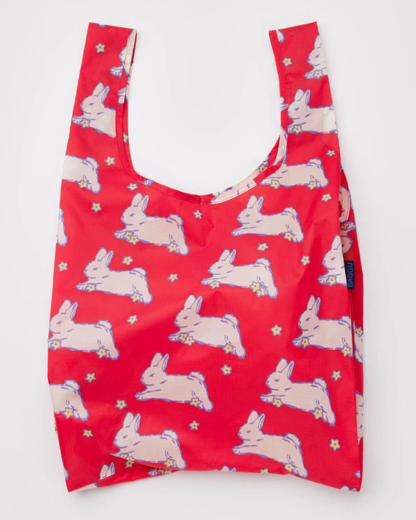 Standard Baggu Einkaufsbeutel Bunnies mit springenden weißen Hasen und gelben Sternen, flach liegend, breite Tragegriffe, kleines Seitenschild BAGGU, aus recyceltem Ripstop-Polyester.