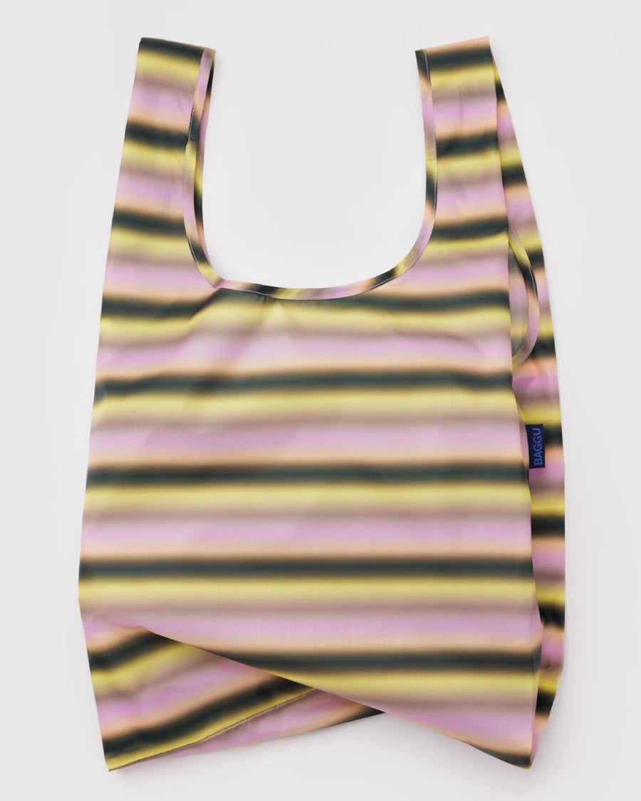Standard Baggu Einkaufsbeutel Gradient Stripe Pink & Yellow, aus recyceltem Ripstop-Polyester, liegt flach. Sichtbar ist ein kleines BAGGU-Markenetikett seitlich.