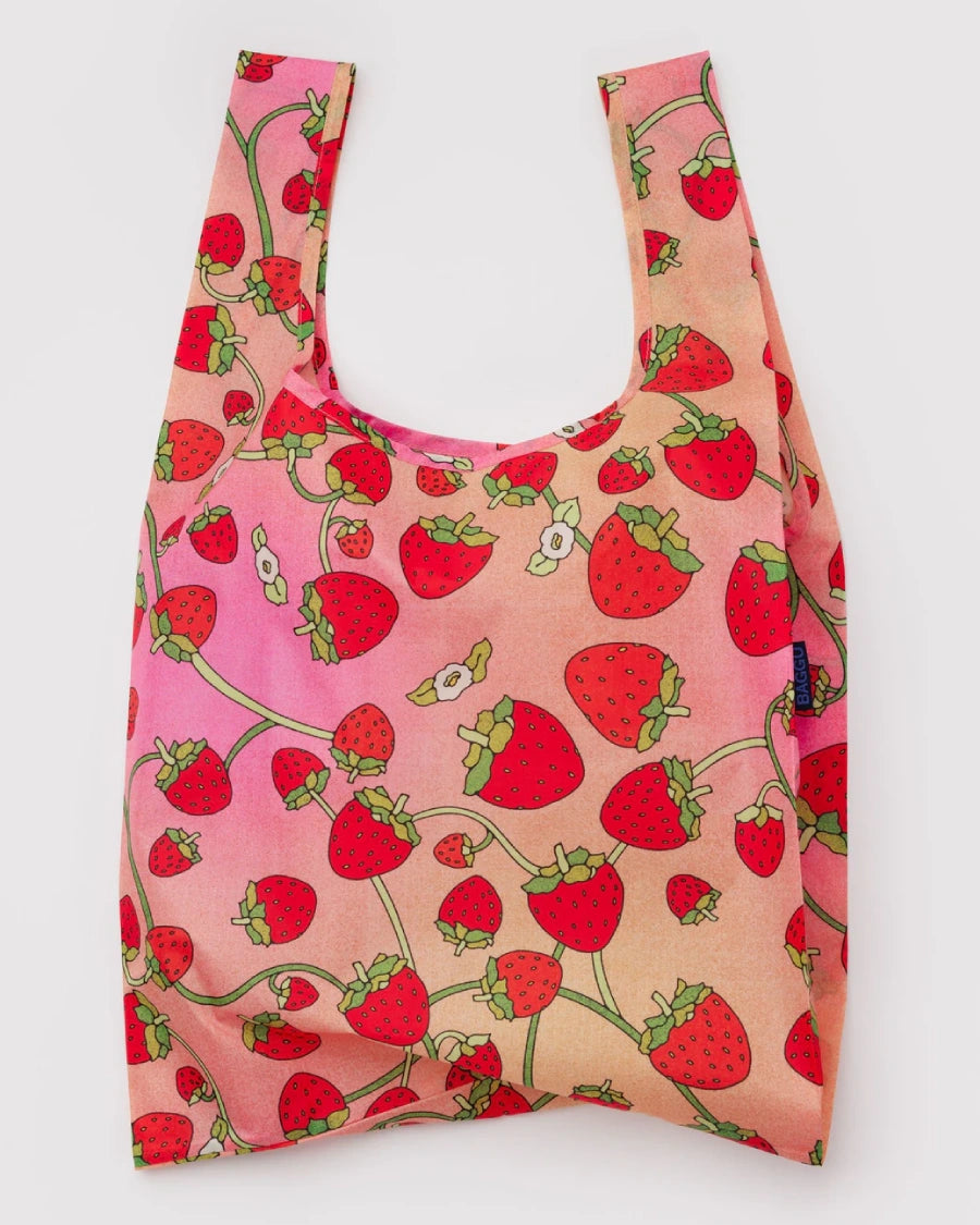 Standard Baggu Einkaufsbeutel Strawberry Blossom, flach gefaltet, mit Erdbeer-Motiv auf rosa- bis pfirsichfarbenem Hintergrund, aus leichtem, recyceltem Ripstop-Polyester, ideal für Einkäufe.