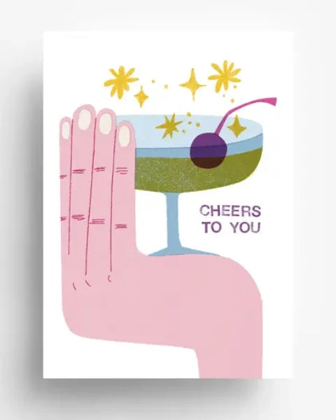 Cheers To You Postkarte mit Illustration einer Hand, die ein Cocktailglas hält, mit goldenem Funkeln und „CHEERS TO YOU“-Text, gedruckt auf ungestrichenem 300g/qm Offsetpapier in Deutschland.