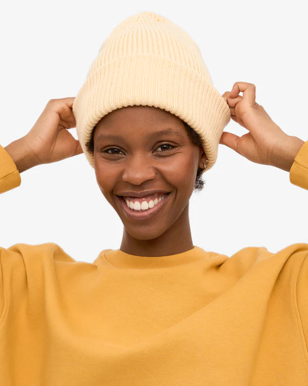 Frau lächelt, trägt Merino Wool Hat Soft Yellow, eine unisex Mütze aus 100% recycelter Merinowolle, passend zum Sweatshirt. Ideal für warme, stilvolle Wintertage.