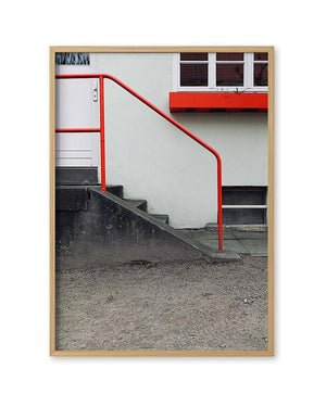 FineArt Print Neighbourhood von Susan Smollich: Fotografie eines Gebäudes mit weißer Wand, rotem Geländer und Tür, in einem schlichten Holzrahmen, signiert und limitiert.
