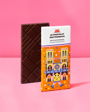 Notre Dame Extra dunkle Schokolade mit Salz aus der Camargue, 70g, mit geometrischen Mustern und Froschmotiv, neben orange-weißer Verpackung mit bunter Kathedralen-Illustration.
