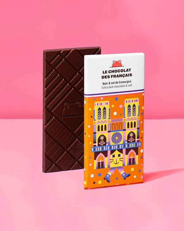 Notre Dame Extra dunkle Schokolade mit Salz aus der Camargue, 70g, mit geometrischen Mustern und Froschmotiv, neben orange-weißer Verpackung mit bunter Kathedralen-Illustration.