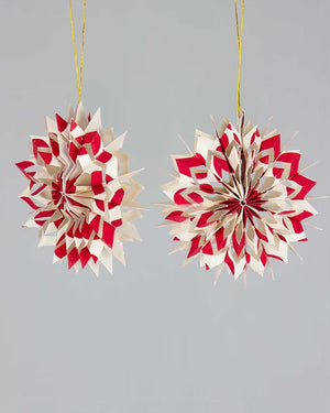 Zwei handgemachte Nova Weihnachtsbaumanhänger aus rot-weißem Baumwollpapier, in 3D-Sternform, von Afroart Studio, an goldenen Fäden hängend.