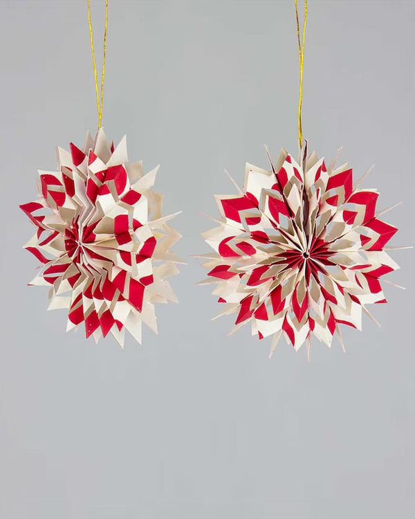 Zwei handgemachte Nova Weihnachtsbaumanhänger aus rot-weißem Baumwollpapier, in 3D-Sternform, von Afroart Studio, an goldenen Fäden hängend.