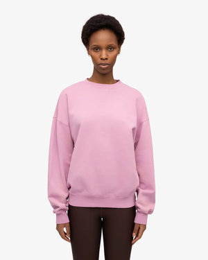 Frau in pastellrosa Organic Oversized Sweatshirt Cherry Blossom aus 100% Bio-Baumwolle, kombiniert mit dunklen Leggings, repräsentiert nachhaltige Mode von Human Empire Shop.