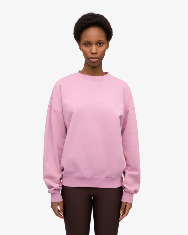 Frau in pastellrosa Organic Oversized Sweatshirt Cherry Blossom aus 100% Bio-Baumwolle, kombiniert mit dunklen Leggings, repräsentiert nachhaltige Mode von Human Empire Shop.