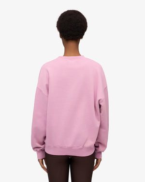Person von hinten in einem locker sitzenden, pastellrosa/lila Oversized Sweatshirt aus Bio-Baumwolle, kombiniert mit dunklen Leggings. Produkt: Organic Oversized Sweatshirt Cherry Blossom.