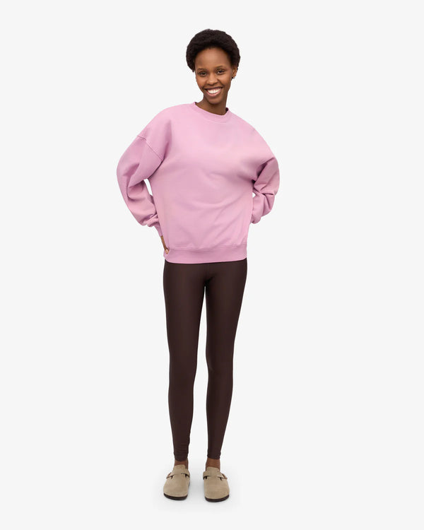 Junge Frau in bequemem Outfit, trägt ein Organic Oversized Sweatshirt Cherry Blossom aus Bio-Baumwolle, passend zu dunklen Leggings und beigen Slip-ons.
