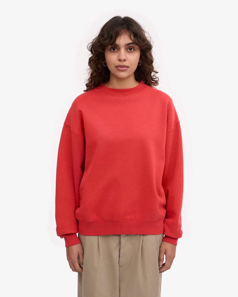 Person trägt den Organic Oversized Sweatshirt Red Tangerine aus 100% Bio-Baumwolle, kombiniert mit weiten, hellen Hosen, schlicht präsentiert für Human Empire Shop.