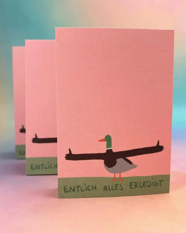 Drei identische Endlich Erledigt Block-Karten mit einem Cartoon-Entenmotiv und dem Text ENDLICH ALLES ERLEDIGT vor einem pinken Hintergrund, klimaneutral auf Recyclingpapier gedruckt.