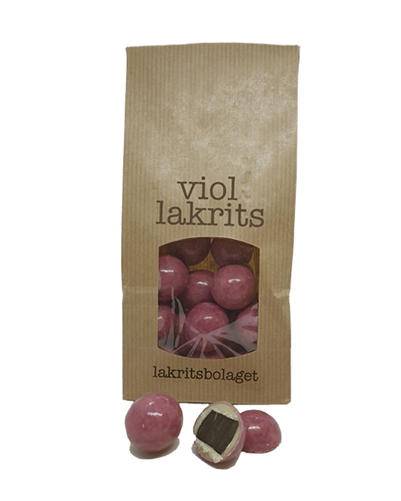 Lakritze mit Veilchen und weißer Schokolade: Kraftpapierbeutel mit violettem Lakritz von lakritsbolaget, sichtbar durch Sichtfenster, mit ausgelegten rosa, glänzenden Kugeln.