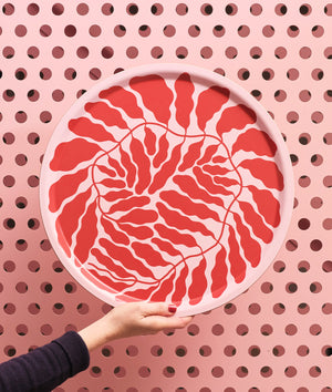 Hand hält das Großes Wrap Red Leaves Tablett Rund, gestaltet von Linnéa Andersson, mit rotem Blattmuster auf rosa Hintergrund, nachhaltig aus Birkensperrholz handgefertigt.
