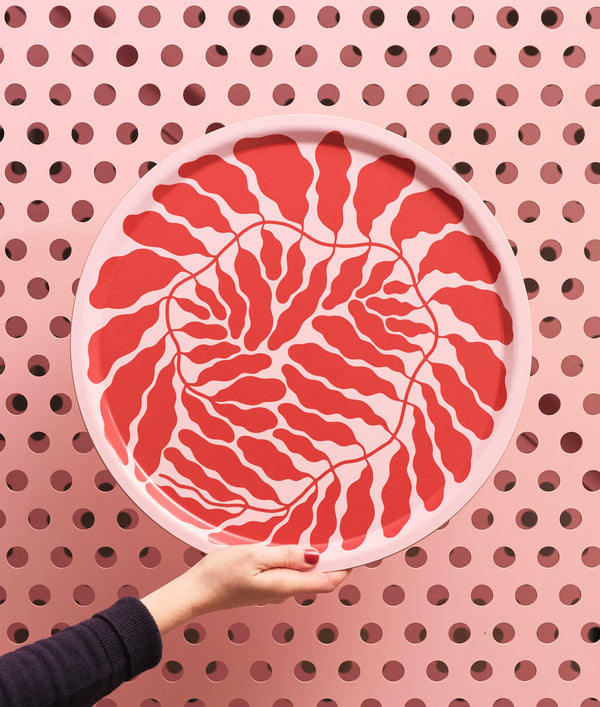 Hand hält das Großes Wrap Red Leaves Tablett Rund, gestaltet von Linnéa Andersson, mit rotem Blattmuster auf rosa Hintergrund, nachhaltig aus Birkensperrholz handgefertigt.